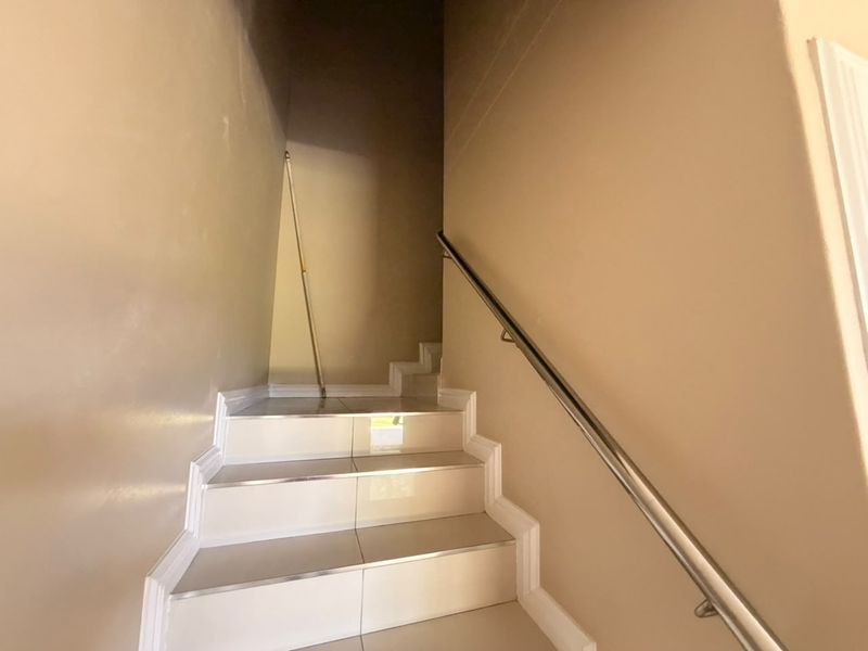 A clean, tiled staircase featuring a modern metal handrail and neutral wall finishes, providing access to the upper level of the townhouse.