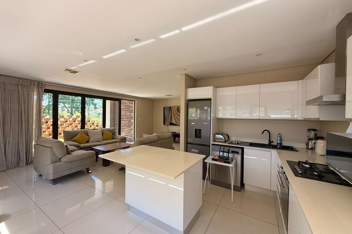 Modern open-plan living area featuring a sleek kitchen with white cabinetry, stone countertops, gas hob, and seamless flow to the outdoor patio area.