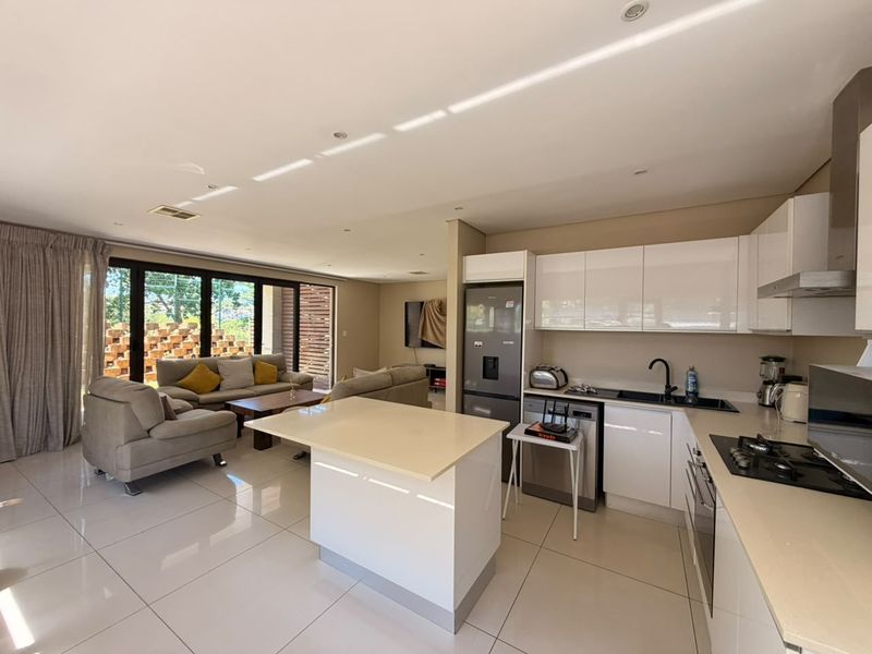 Modern open-plan living area featuring a sleek kitchen with white cabinetry, stone countertops, gas hob, and seamless flow to the outdoor patio area.