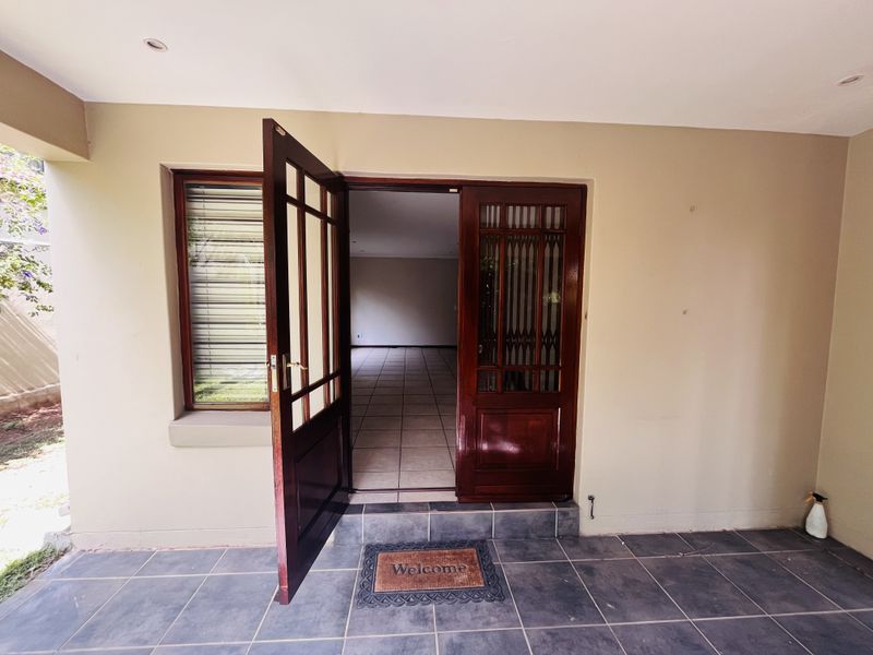 A covered entrance area featuring dark wood doors, tiled flooring, and recessed lighting, leading into an open-plan interior space.