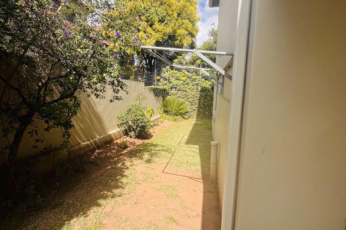 A narrow rear garden area featuring a wall-mounted clothesline, downpipe, and boundary wall with established greenery.