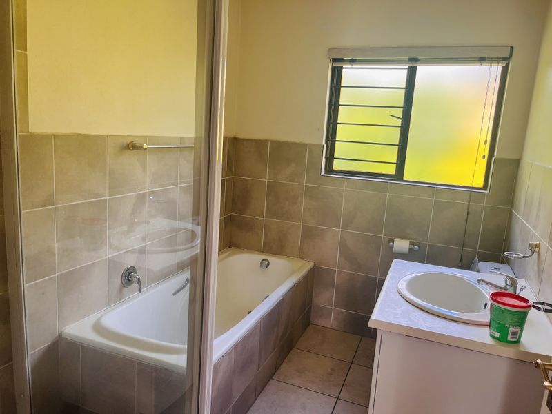 A functional bathroom featuring a built-in bathtub, a vanity with a drop-in sink, and neutral wall and floor tiling.