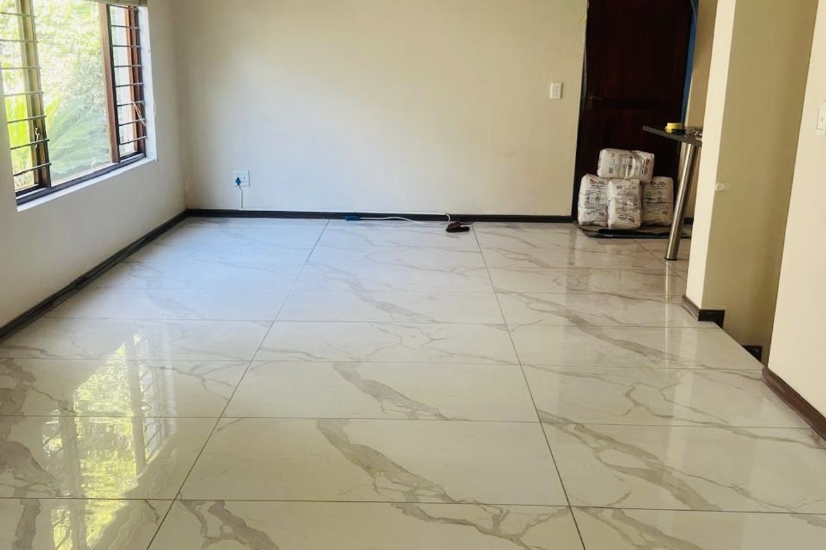 A bright, vacant living area featuring modern large-format marble-look floor tiles, recessed lighting, and large windows, currently undergoing minor finishing touches.