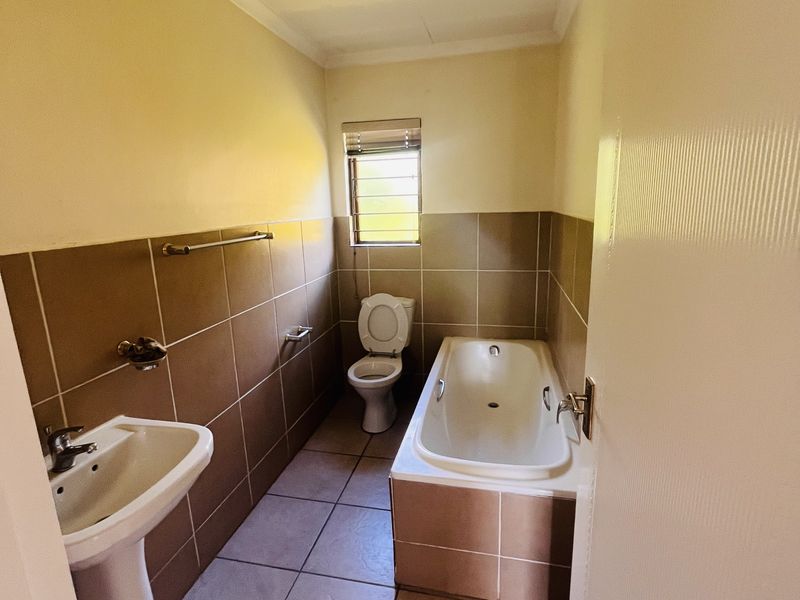 A functional bathroom featuring a pedestal basin, built-in bathtub, and toilet with neutral wall and floor tiling.