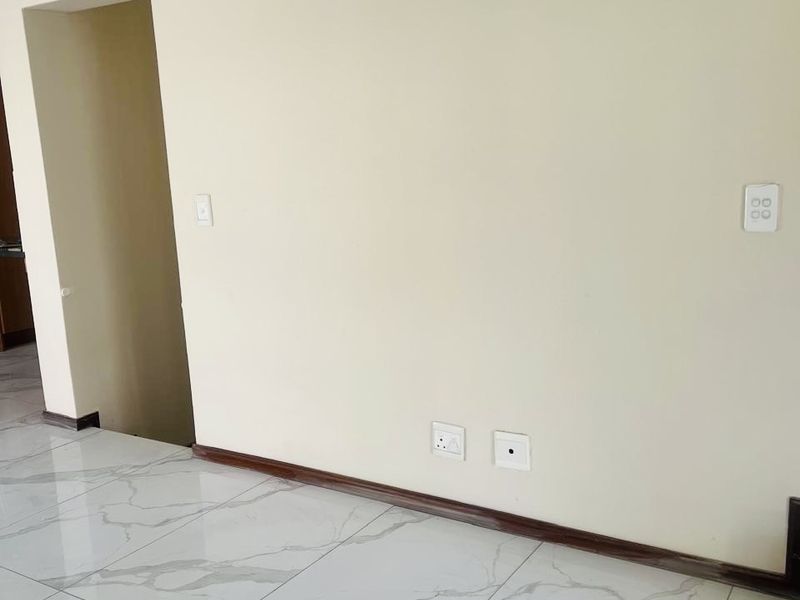 A bright, empty living area featuring modern marble-look porcelain floor tiles, neutral wall finishes, and integrated electrical points.