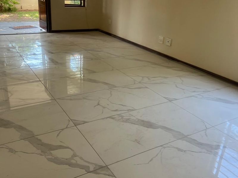 A bright, empty living area featuring modern marble-look porcelain floor tiles, neutral walls, and direct access to an outdoor patio through a glass-paneled door.