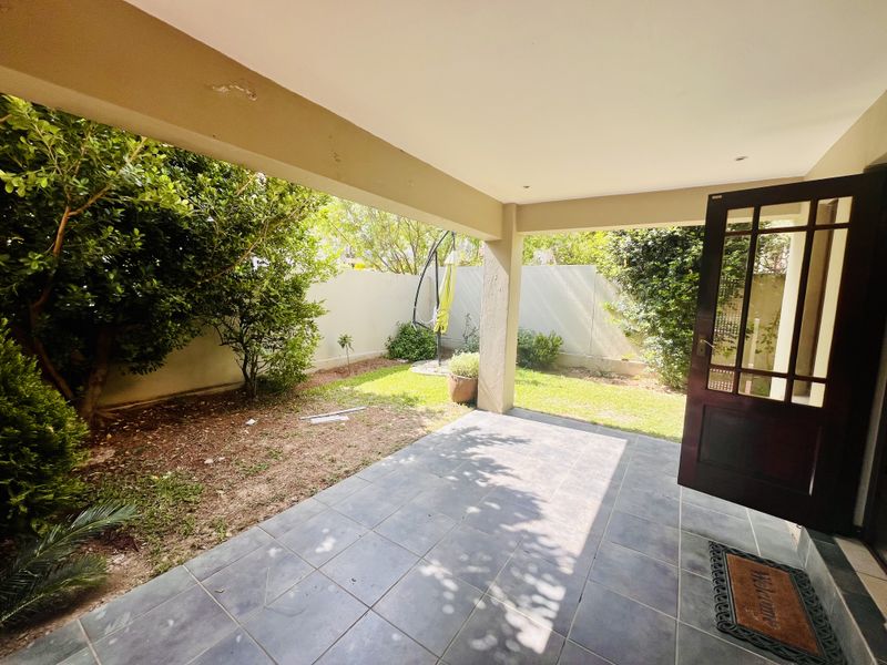 A covered patio area featuring tiled flooring and recessed lighting, opening onto a private garden space with boundary walls.