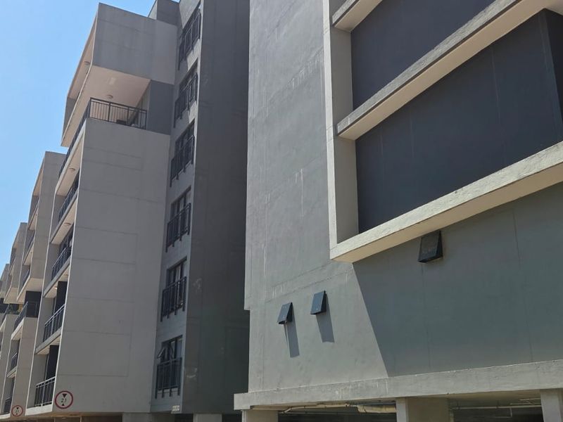 A modern multi-story apartment building facade featuring clean concrete lines, dark grey accents, and private balconies with metal railings.