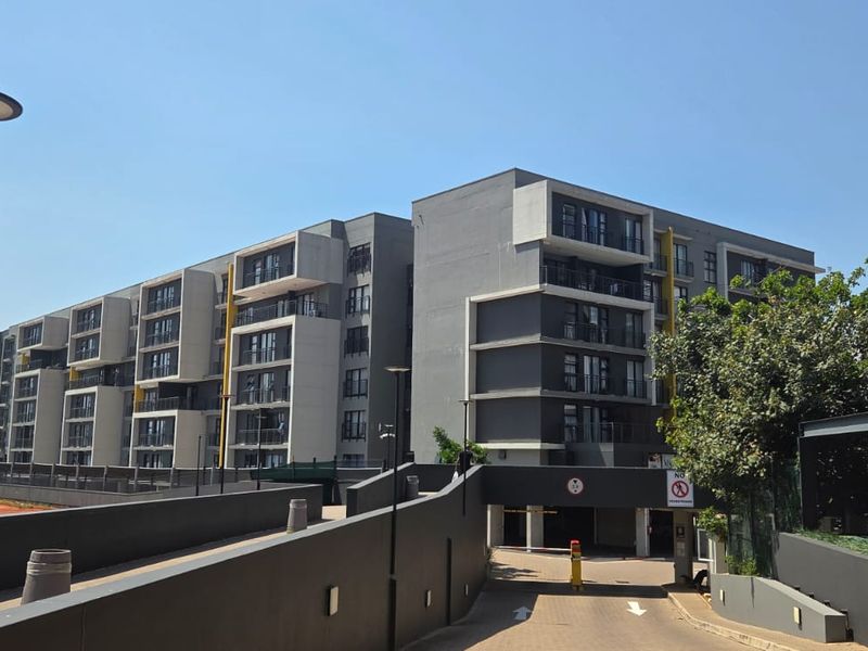 Modern multi-story apartment complex featuring a secure underground parking entrance, contemporary facade design, and well-maintained surrounding infrastructure.