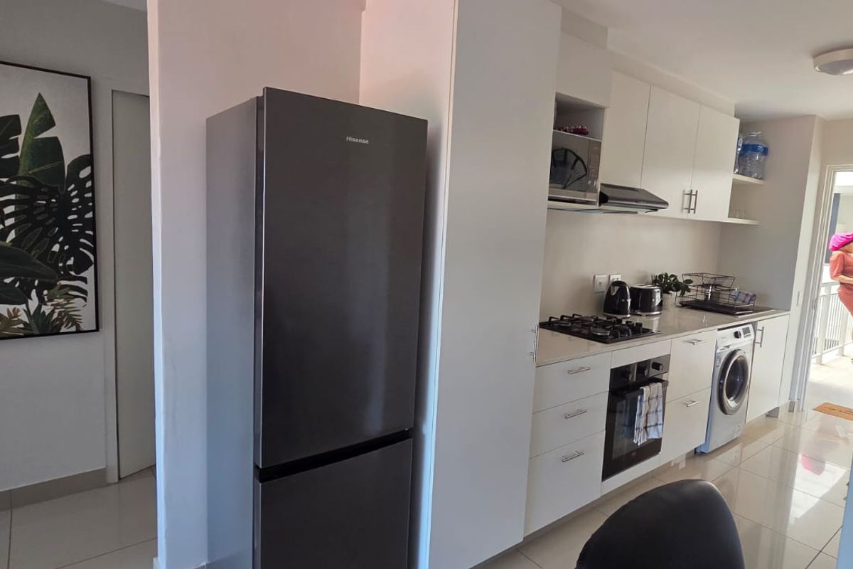 Modern kitchen featuring white cabinetry, stone countertops, gas hob, built-in oven, extractor fan, and integrated laundry appliance with sleek tiled flooring.