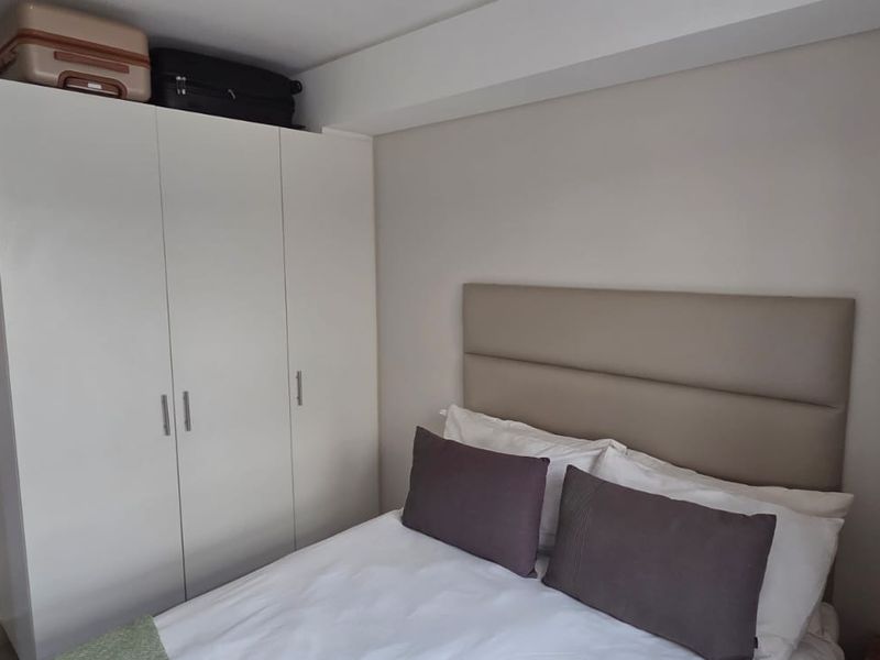 A well-maintained bedroom featuring a built-in wardrobe, neutral wall finishes, and a modern upholstered headboard, with direct access to an adjacent balcony area.