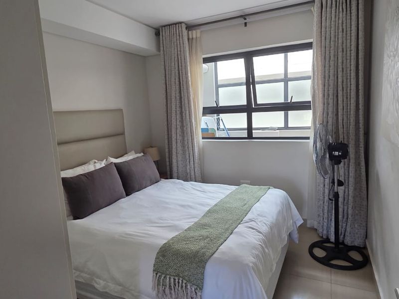 A well-maintained bedroom featuring tiled flooring and large aluminium-framed windows with integrated curtain tracks, providing natural light and a neutral aesthetic.