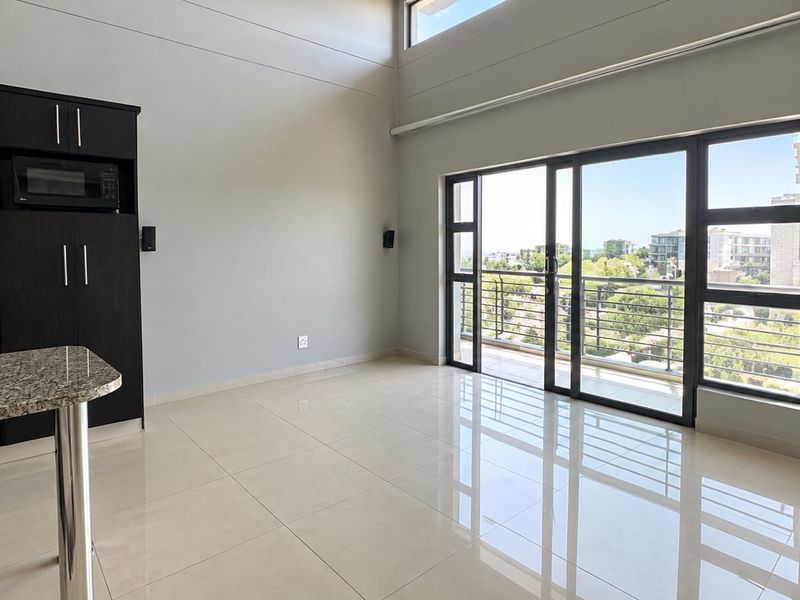 Spacious open-plan living area featuring sleek tiled floors, modern built-in kitchen cabinetry, and large sliding doors opening to a balcony with scenic views.