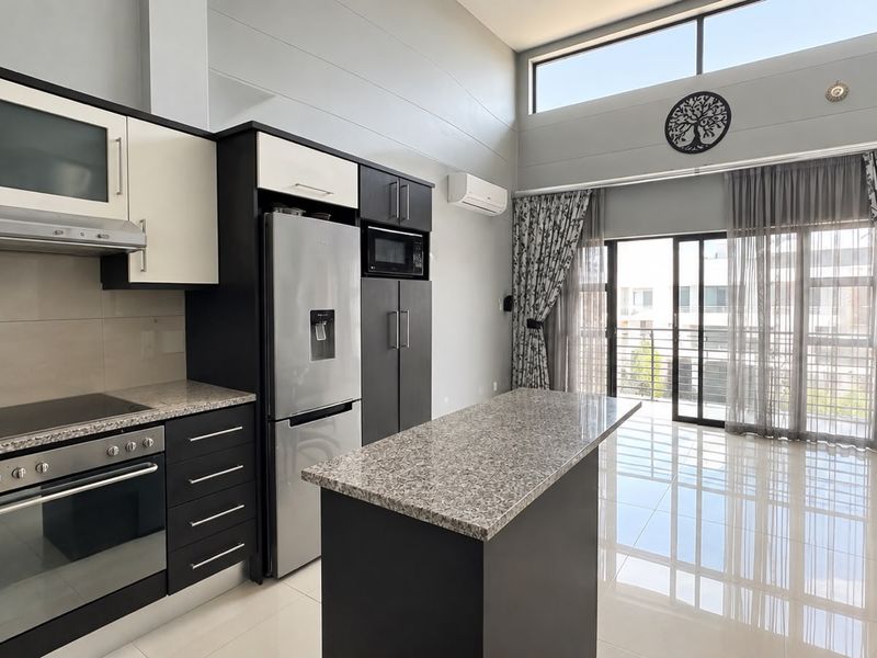 Modern open-plan kitchen and living area featuring sleek cabinetry, granite countertops, high ceilings, and large sliding doors leading to a balcony.