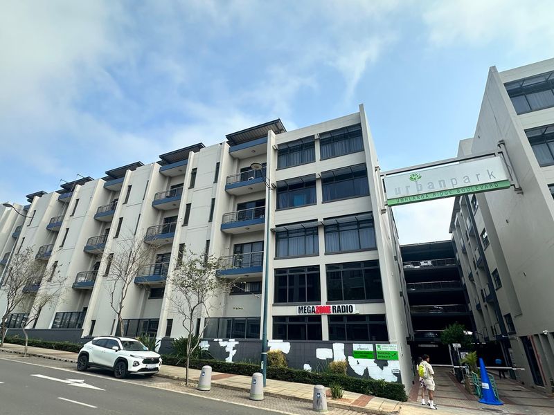 Exterior view of the Urban Park apartment building featuring a multi-story facade with balconies, large windows, and a ground-level parking garage entrance.