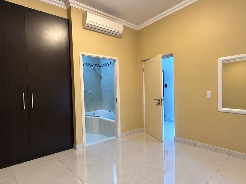 Spacious bedroom featuring tiled flooring, built-in cupboards, and a split-system air conditioner, with direct access to an en-suite bathroom.