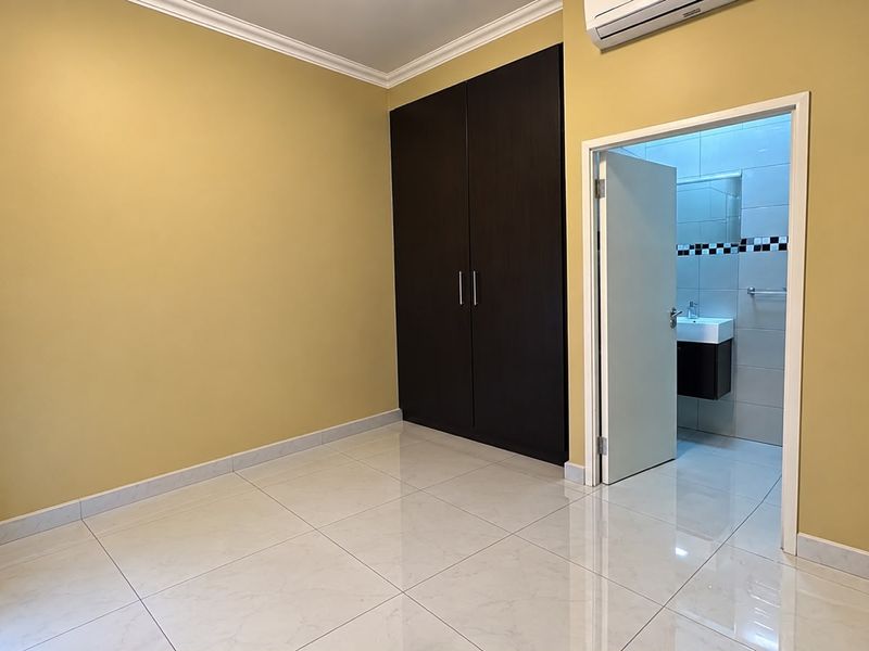 A clean, empty bedroom featuring tiled flooring, a dark wood built-in wardrobe, air conditioning, and direct access to an en-suite bathroom.