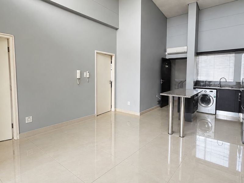 Spacious open-plan living area featuring high ceilings, tiled floors, and a modern kitchen with granite breakfast counter and integrated laundry plumbing.