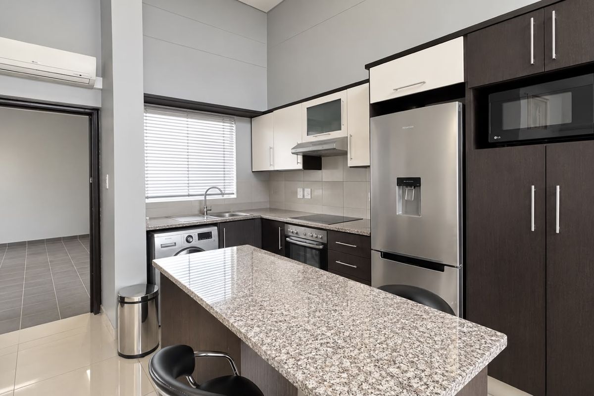 Modern kitchen featuring granite countertops, built-in oven, hob, extractor fan, and integrated microwave, complemented by sleek dark and light cabinetry.