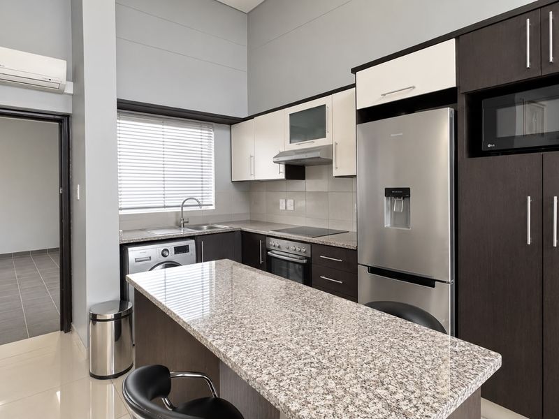 Modern kitchen featuring granite countertops, built-in oven, hob, extractor fan, and integrated microwave, complemented by sleek dark and light cabinetry.