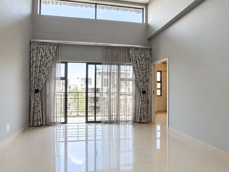 Spacious living area featuring double volume ceilings, clerestory windows, and large sliding doors leading to a balcony with polished porcelain tile flooring.