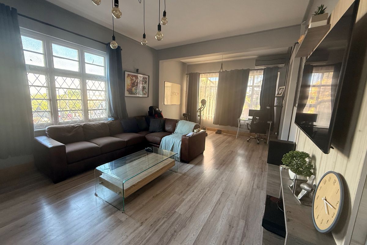 Spacious living room featuring light-toned laminate flooring, large leaded glass windows, and a wall-mounted air conditioning unit.