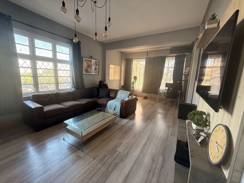 Spacious living room featuring light-toned laminate flooring, large leaded glass windows, and a wall-mounted air conditioning unit.