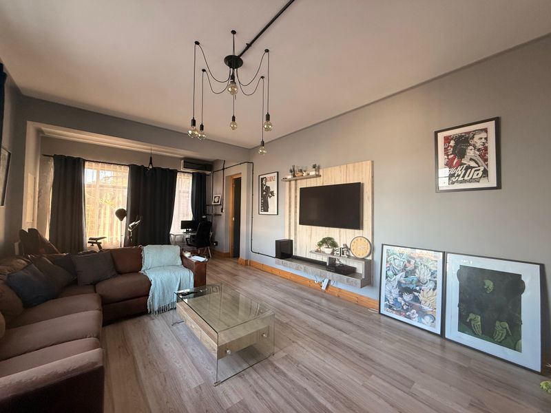 A well-maintained living room featuring modern laminate flooring, a wall-mounted media console, and industrial-style exposed conduit lighting.