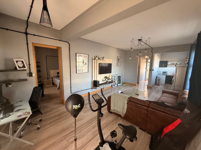 Spacious open-plan living area featuring laminate flooring, exposed conduit lighting, and a modern kitchen with subway tile backsplash and integrated cabinetry.