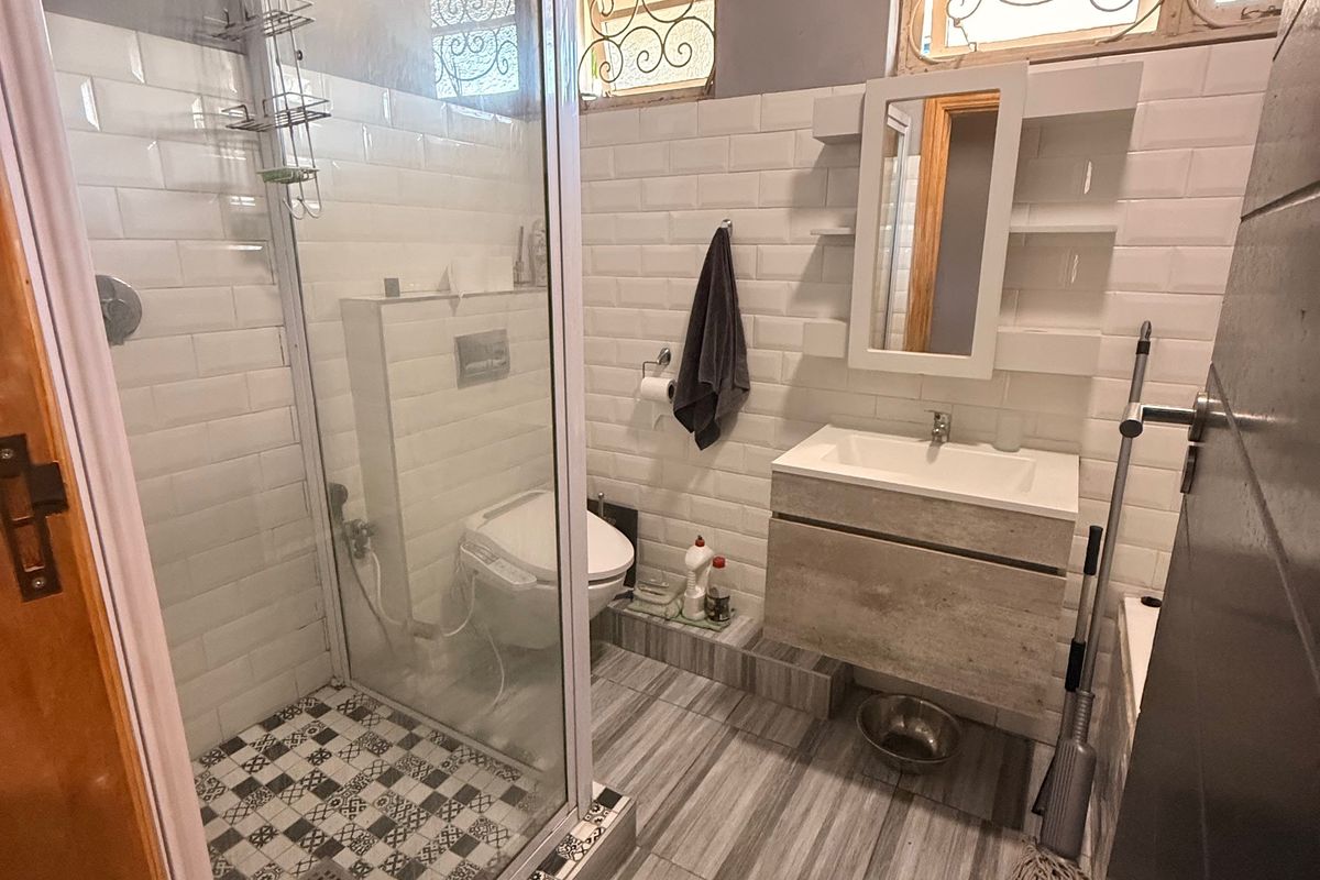 A compact bathroom featuring a glass-enclosed shower, floating vanity, and subway tile wall finishes with decorative floor tiling.