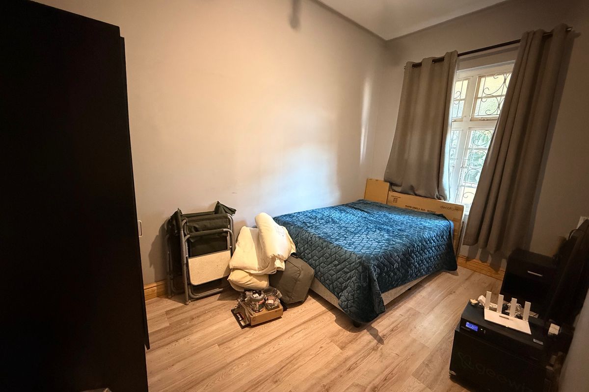 A bedroom featuring light-toned laminate flooring and a window fitted with security bars, offering a functional space ready for personalization.