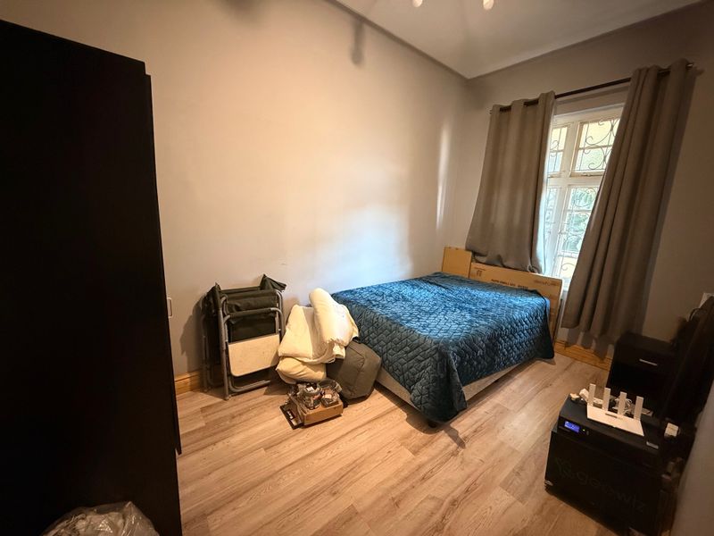 A bedroom featuring light-toned laminate flooring and a window fitted with security bars, offering a functional space ready for personalization.