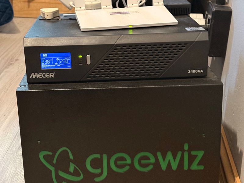 A portable power backup unit and router placed on the floor in an indoor setting.