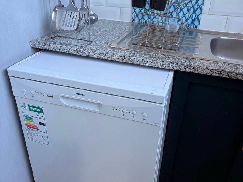 A compact kitchen area featuring a granite countertop, subway tile backsplash, stainless steel sink, and a white freestanding dishwasher.