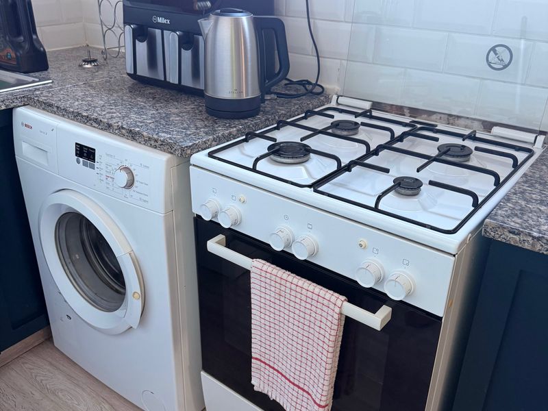 Compact kitchen area featuring a gas stove, built-in oven, integrated washing machine, granite countertops, and a classic white subway tile backsplash.