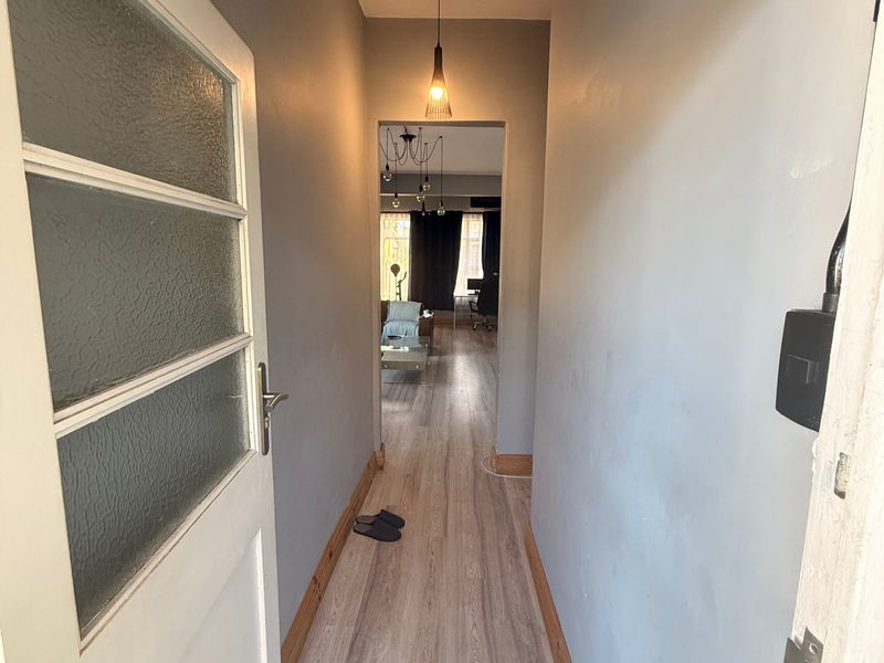 A narrow hallway featuring light-toned laminate flooring, grey painted walls, and a modern pendant light fixture leading into the main living area.