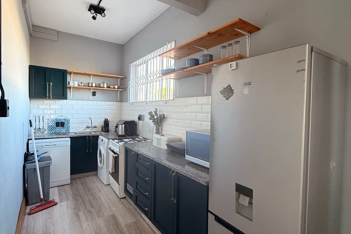 A functional galley-style kitchen featuring dark cabinetry, subway tile backsplash, stone countertops, and light wood-look laminate flooring.