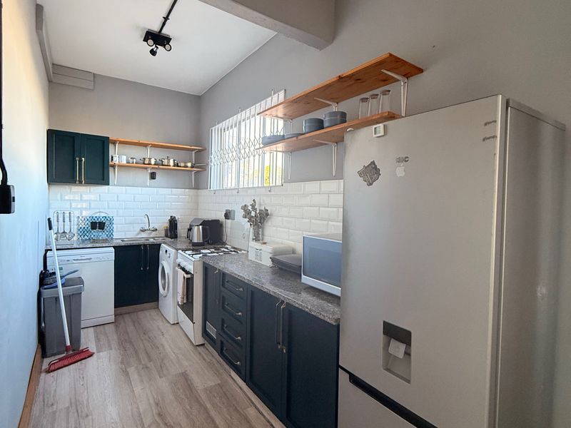 A functional galley-style kitchen featuring dark cabinetry, subway tile backsplash, stone countertops, and light wood-look laminate flooring.