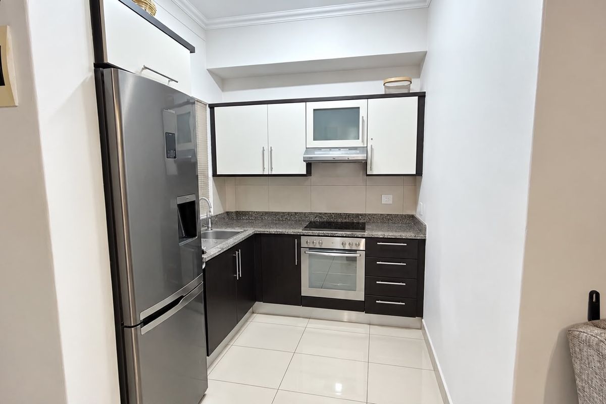 A modern, compact kitchen featuring dark and white cabinetry, granite countertops, and integrated stainless steel appliances with clean tiled flooring.