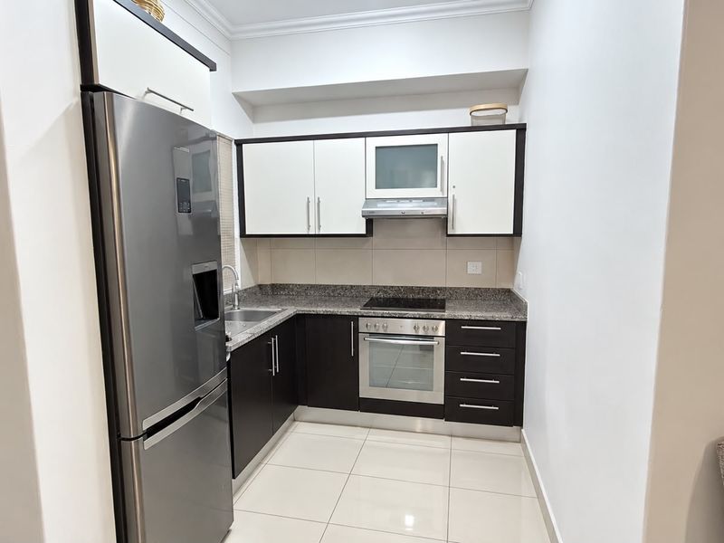 A modern, compact kitchen featuring dark and white cabinetry, granite countertops, and integrated stainless steel appliances with clean tiled flooring.