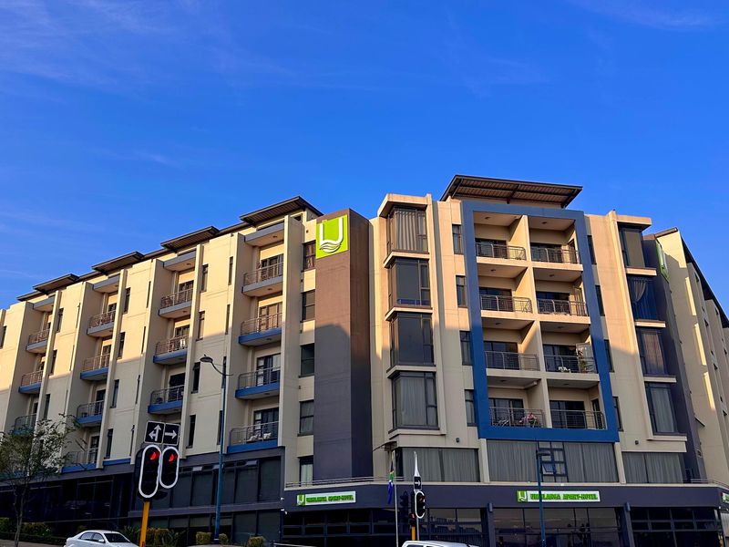 A modern multi-story apartment building featuring a contemporary facade with balconies, large windows, and prominent signage under a clear blue sky.