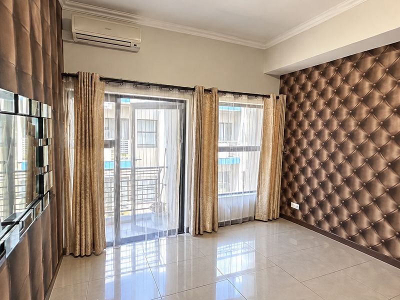 A bright, empty living room featuring tiled floors, decorative tufted wall paneling, and direct access to a private balcony through sliding glass doors.