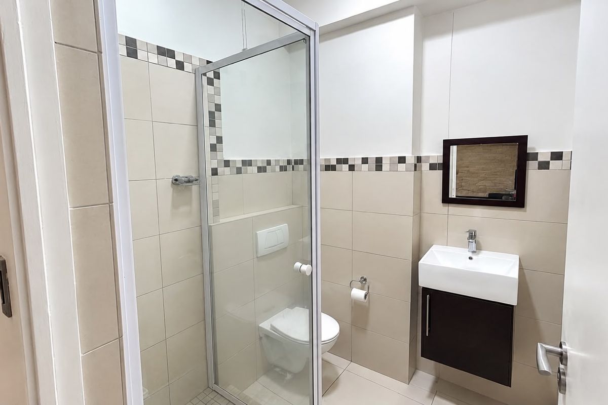 A clean, modern bathroom featuring a glass-enclosed shower, wall-mounted toilet, and a sleek vanity basin with storage.