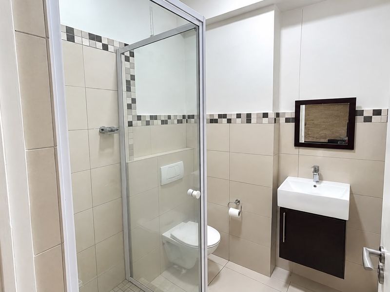 A clean, modern bathroom featuring a glass-enclosed shower, wall-mounted toilet, and a sleek vanity basin with storage.