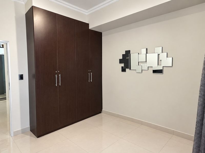 A clean, modern bedroom featuring dark wood built-in cupboards, neutral tiled flooring, and crisp white walls.