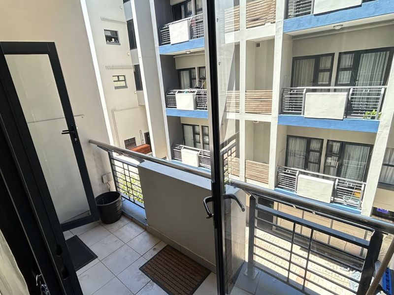 A compact apartment balcony featuring tiled flooring and a metal balustrade, overlooking the building's central courtyard area.