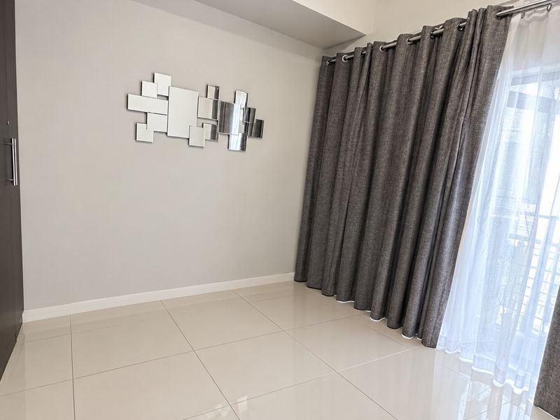 A bright, empty bedroom featuring neutral tiled flooring, a built-in wardrobe, and floor-to-ceiling curtains leading to a balcony.