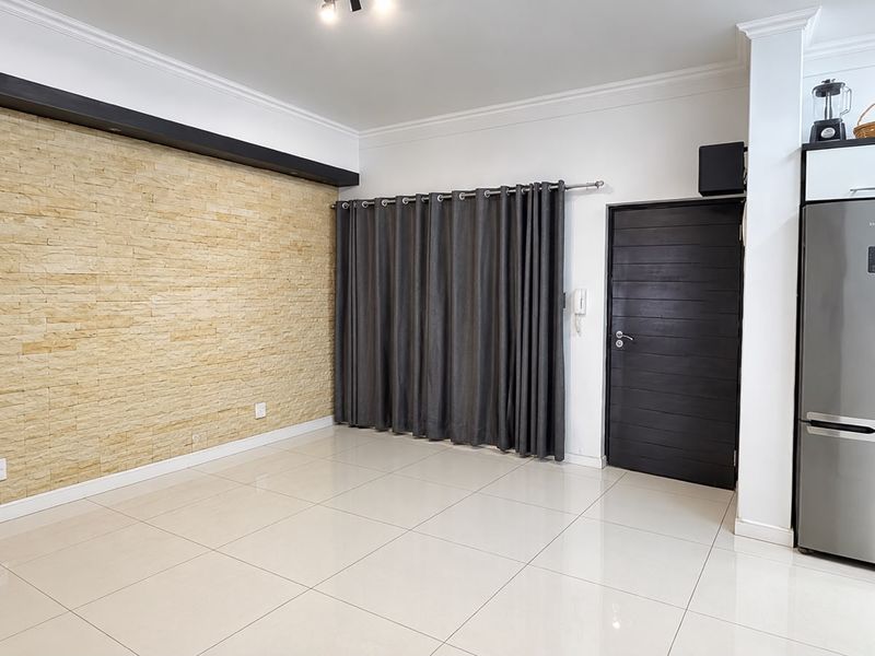 Spacious open-plan living area featuring a textured stone accent wall, neutral tiled flooring, and modern finishes, offering a versatile layout for contemporary living.