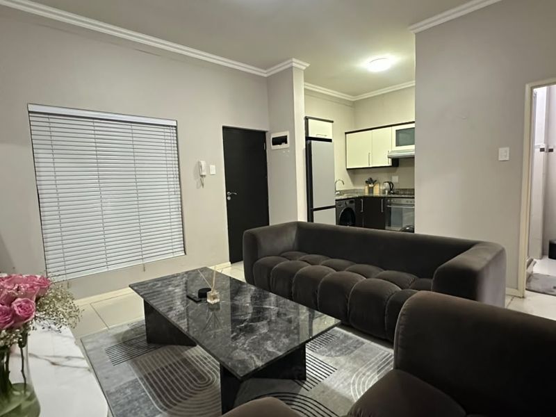An open-plan living area featuring a modern kitchen with built-in cabinetry and appliances, adjacent to a bathroom with a vanity unit.