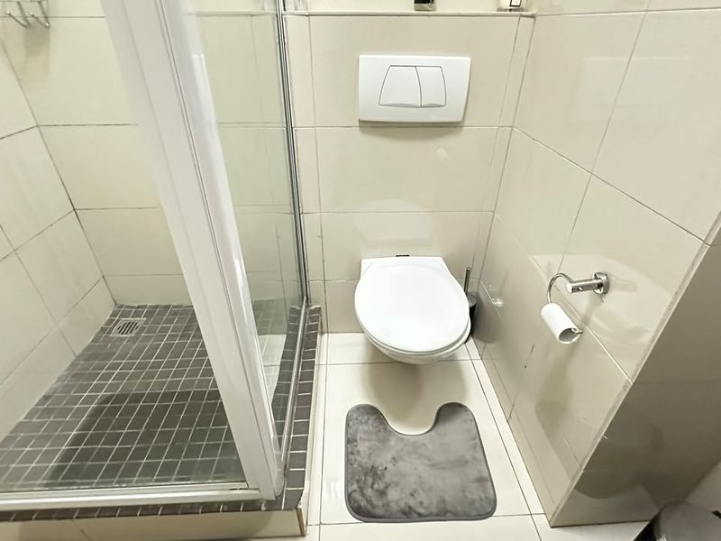 A compact, modern bathroom featuring a wall-mounted toilet and a glass-enclosed shower with neutral tiled finishes.